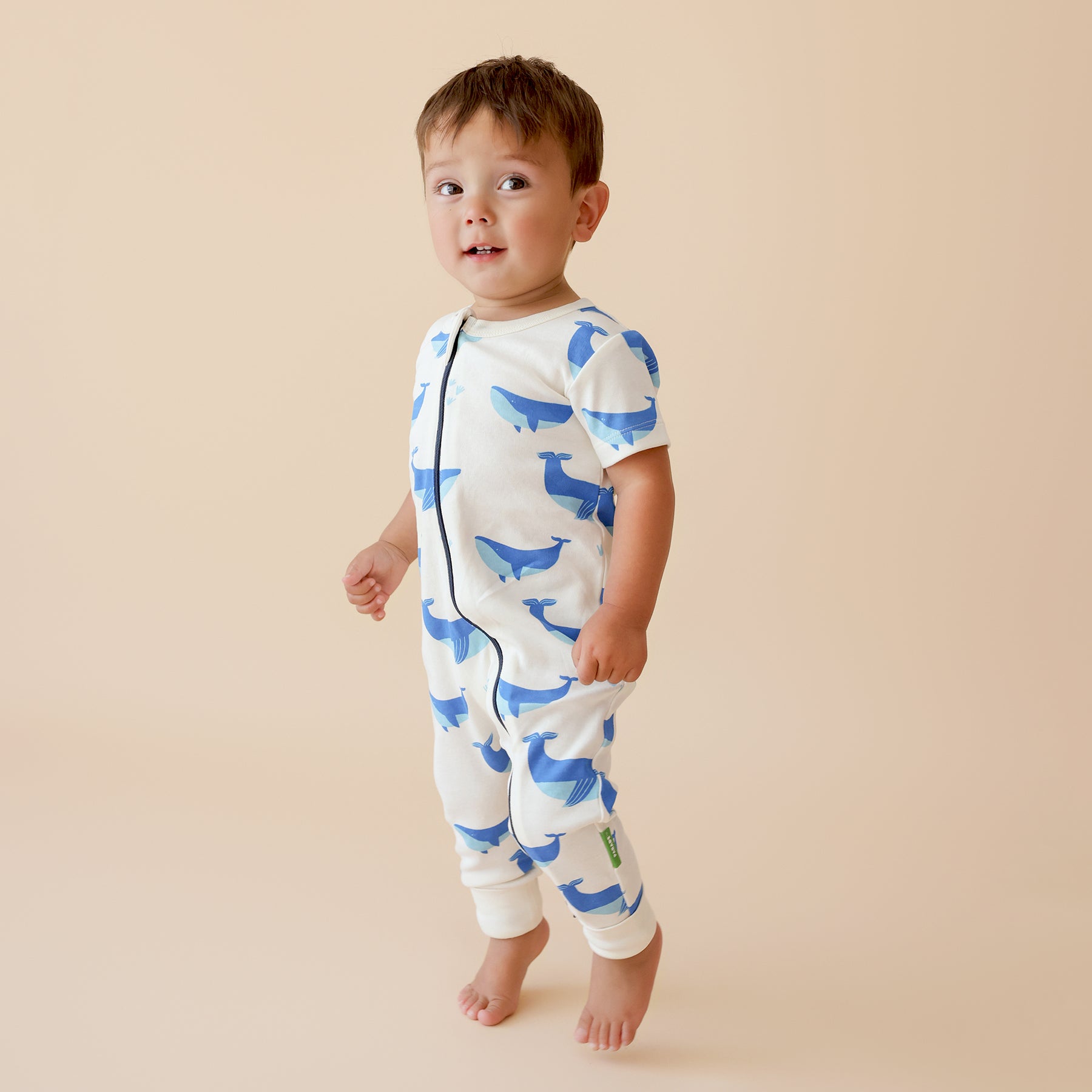 Child wearing a white zipper romper with blue whale patterns on a beige background